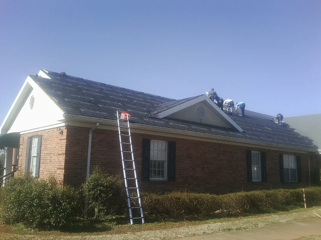 Crew tearing shingles off a brick ranch roof with a ladder set — Emergency Roof Repair work by our crew in Sacramento