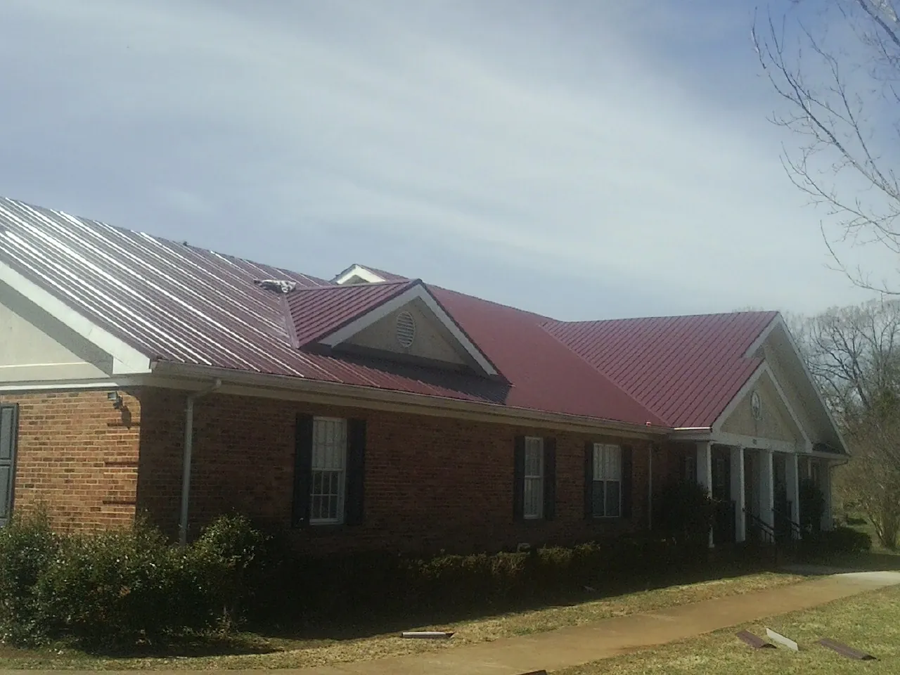 Red metal roof with gabled entries on a long brick building, from a Hail Damage Roof Repair job in Sacramento