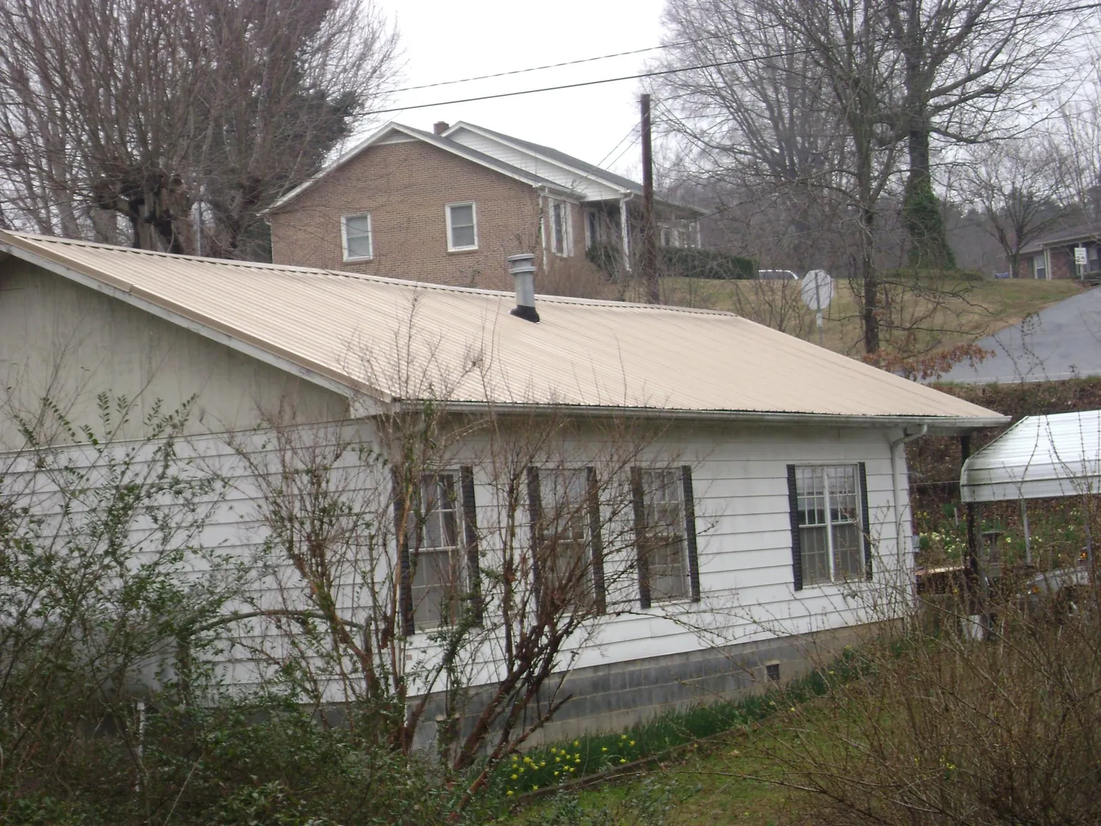 Tan metal roof on a white sided house set into a hillside — Commercial Roofing by Roofing Brothers in Sacramento